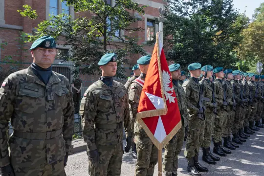 Żołnierze w mundurach wojskowych z flagą Polski podczas ceremonii.