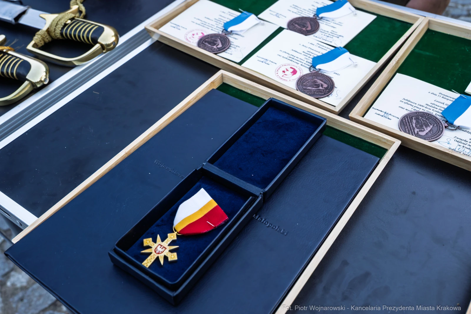 Medal z wstążką w kolorach narodowych oraz dyplomy i medale na tle.  Autor: Piotr Wojnarowski