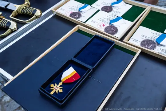 Medal z wstążką w kolorach narodowych oraz dyplomy i medale na tle.
