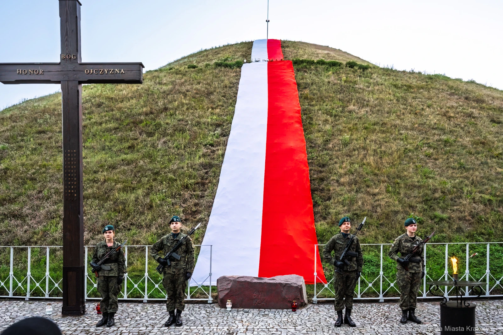 Żołnierze stojący na tle wzgórza z biało-czerwoną flagą.  Autor: Piotr Wojnarowski