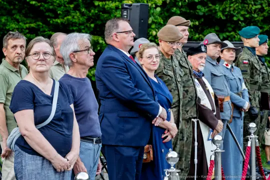 Grupa ludzi w różnych strojach, w tym mundurach wojskowych, podczas uroczystości.