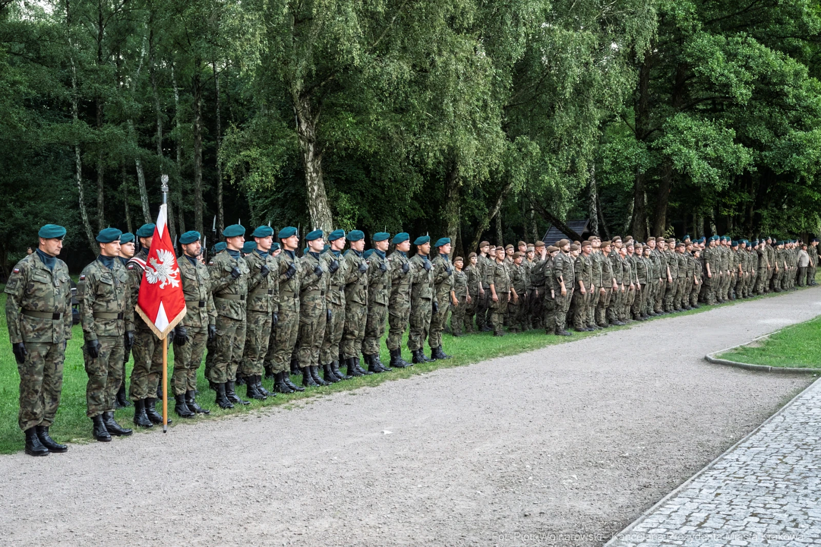 Żołnierze w mundurach stoją w szeregu, trzymając flagę. Drzewa w tle.  Autor: Piotr Wojnarowski
