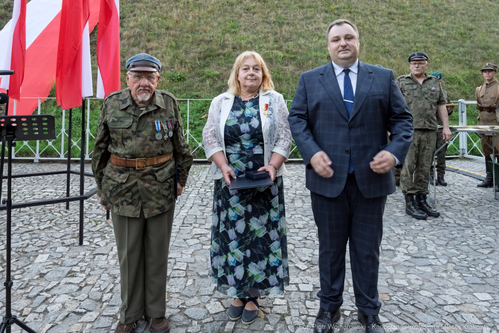 Uroczystość z udziałem dwóch mężczyzn w mundurach i kobiety w sukience, flagi w tle.  Autor: Piotr Wojnarowski