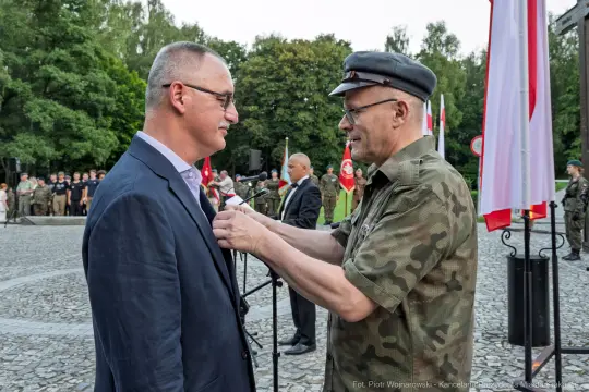 Ceremonia wręczenia odznaczenia wojskowego. Mężczyzna w mundurze przypina medal do marynarki innego mężczyzny.