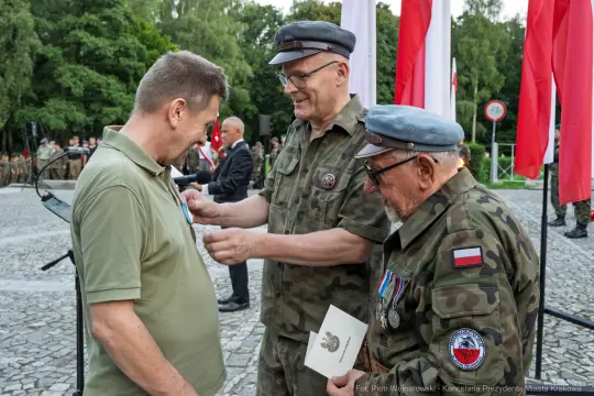 Wręczenie odznaczenia weteranowi przez dwóch mężczyzn w mundurach wojskowych.