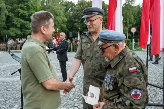 Uroczystość wręczenia odznaczeń w obecności żołnierzy i flag narodowych.
