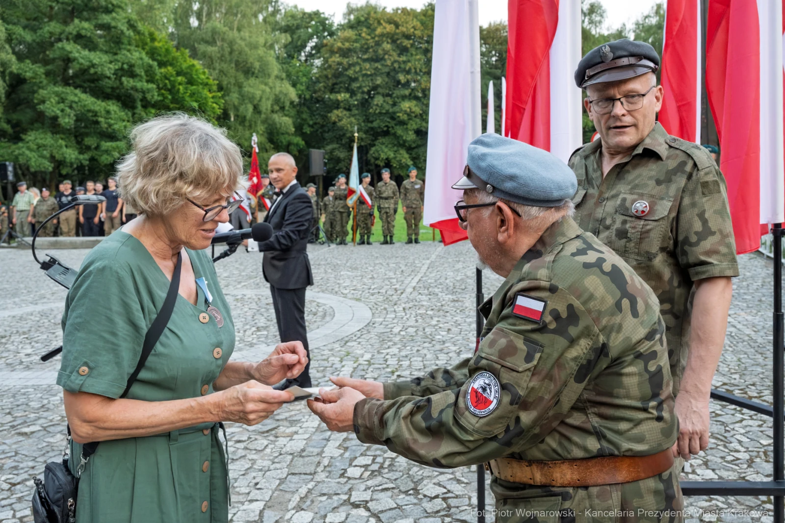 Wręczenie odznaczenia przez weterana kobiecie w mundurze, w tle flagi Polski i zgromadzenie ludzi.  Autor: Piotr Wojnarowski