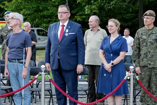 Grupa ludzi w formalnych strojach podczas uroczystości na świeżym powietrzu.