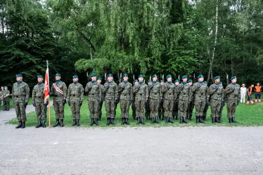 Żołnierze w mundurach wojskowych stoją w szeregu, trzymając flagę.