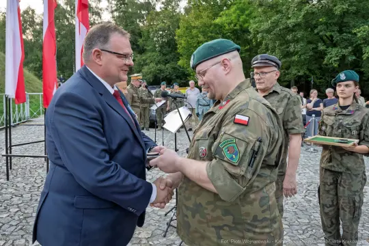 Wręczenie odznaczenia wojskowego w obecności żołnierzy i flag narodowych.