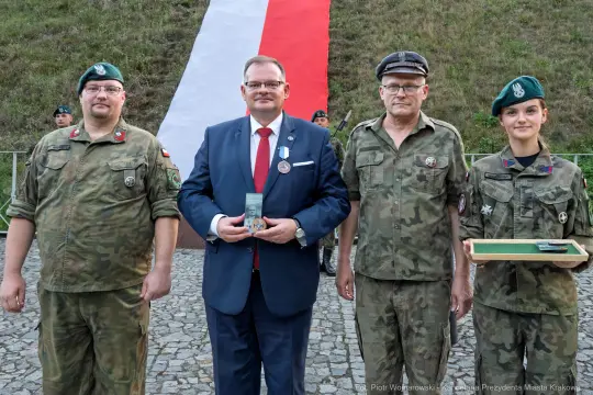 Uroczystość wręczenia medali w mundurach wojskowych z flagą Polski w tle.