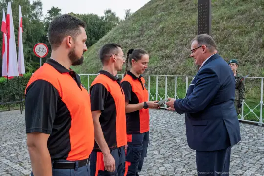 Wręczenie nagrody przez mężczyznę w garniturze grupie osób w pomarańczowych koszulach.