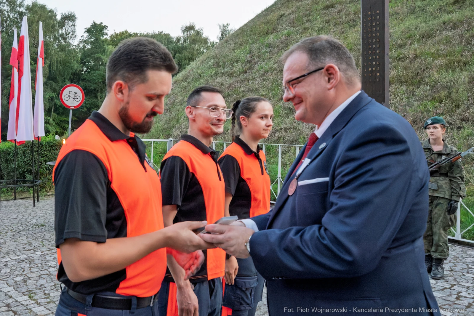 Uroczystość wręczenia odznaczeń przez przedstawiciela władz. Czerwone kamizelki, flagi Polski w tle.  Autor: Piotr Wojnarowski