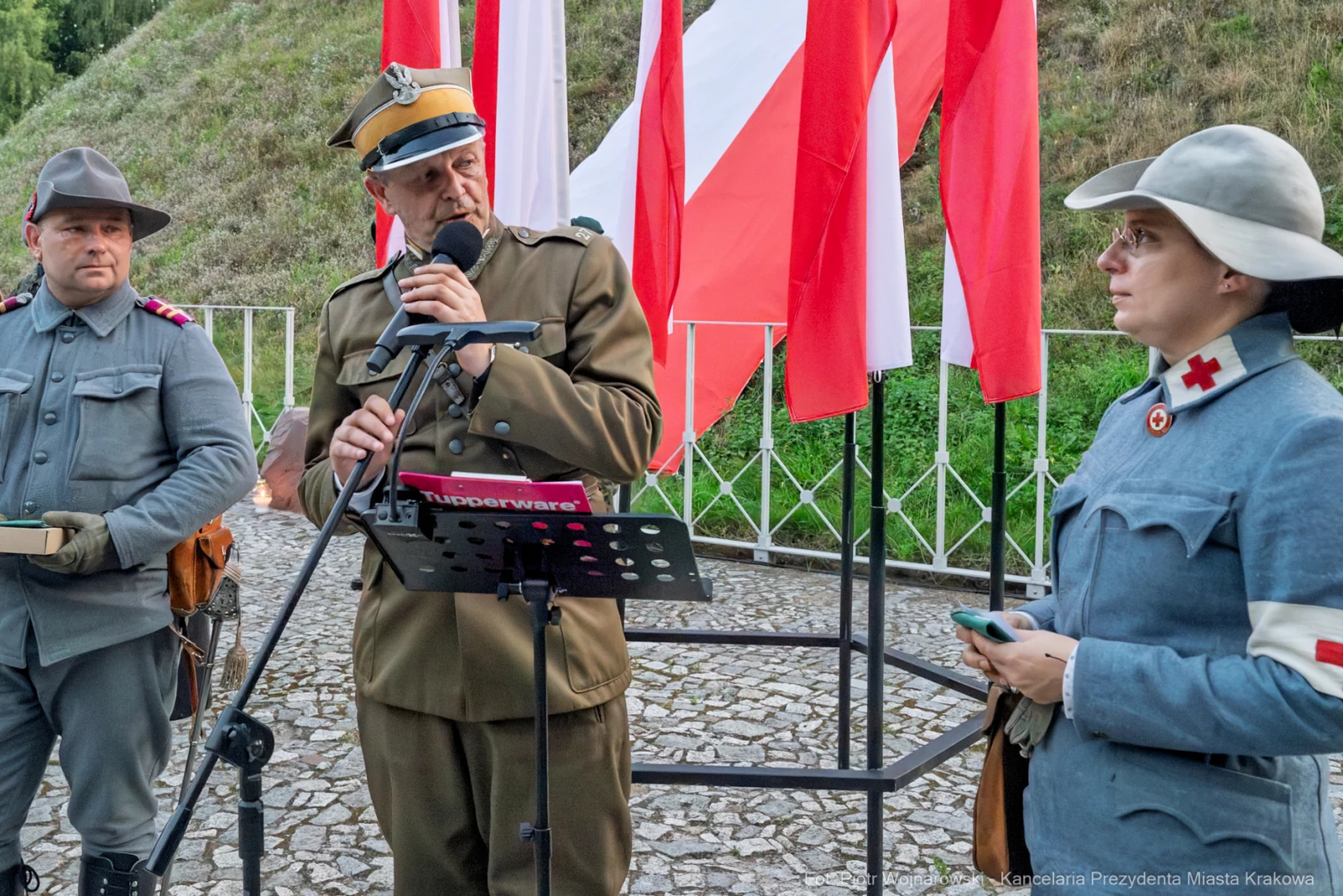 Mężczyzna w mundurze przemawia do mikrofonu, obok niego żołnierz i kobieta w mundurze z czerwonym krzyżem.  Autor: Piotr Wojnarowski