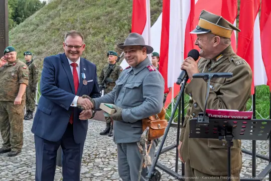 Uroczystość z udziałem żołnierzy, wręczenie nagrody, flagi Polski w tle.