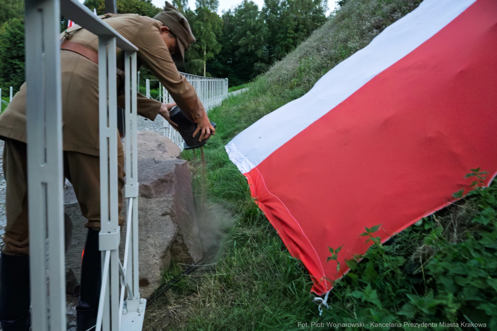 Mężczyzna w mundurze zasypuje kamień przy polskiej fladze.  Autor: Piotr Wojnarowski