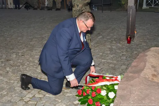 Mężczyzna w garniturze składa wieniec na cześć zmarłych.