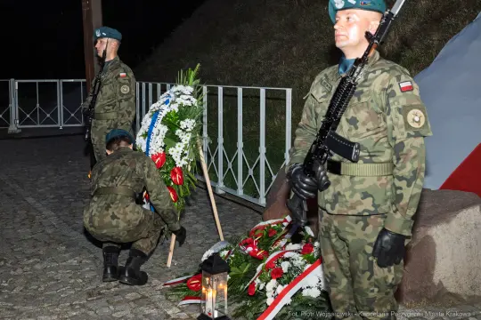 Żołnierze składają wieńce w hołdzie, obok zniczy i flagi narodowej.
