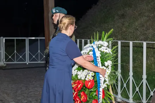 Kobieta składa wieniec na tle żołnierza w mundurze.