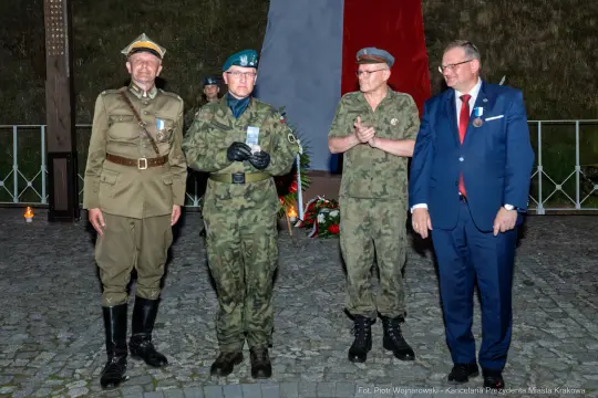 Czterech mężczyzn w mundurach wojskowych i cywilnych, stojących obok siebie, z odznaczeniami.