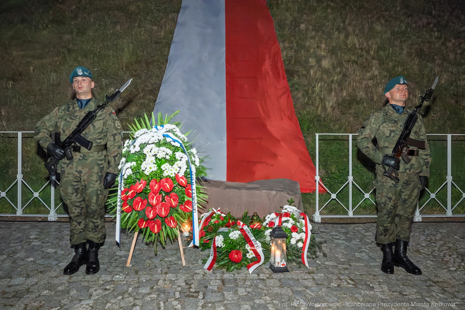 Żołnierze w mundurach stoją przy pomniku z kwiatami i zniczem, w tle flaga Polski.  Autor: Piotr Wojnarowski