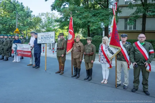 Uczestnicy marszu z flagami i transparentami, w mundurach historycznych.