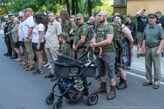 Grupa ludzi w mundurach wojskowych i cywilnych, niektórzy z dziećmi w wózkach.