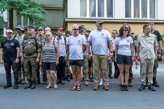 Grupa ludzi w koszulkach, stojących w szeregu na ulicy, w różnorodnych strojach.