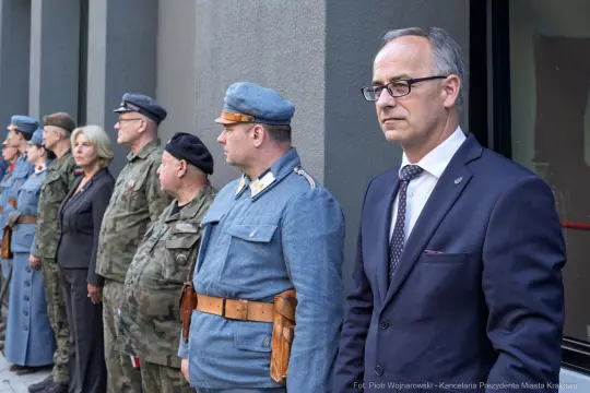 Grupa osób w mundurach i eleganckich strojach, stojących w szeregu podczas uroczystości.