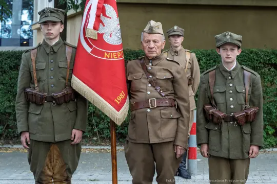 Grupa żołnierzy w mundurach historycznych z flagą.