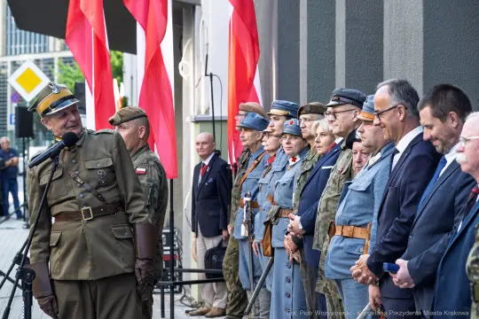 Uroczystość z udziałem żołnierzy i przedstawicieli władz, flagi Polski w tle.