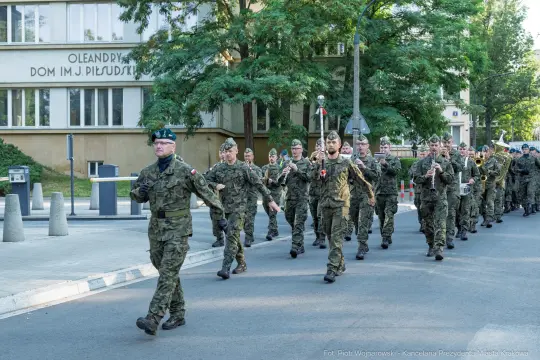 Żołnierze w mundurach maszerujący ulicą, grający na instrumentach muzycznych.