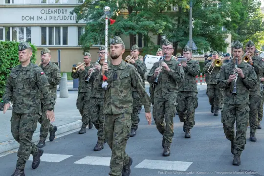 Żołnierze w mundurach wojskowych maszerują z instrumentami muzycznymi.