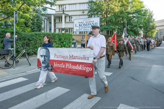 Marsz z transparentem upamiętniającym Józefa Piłsudskiego, uczestnicy w mundurach historycznych.