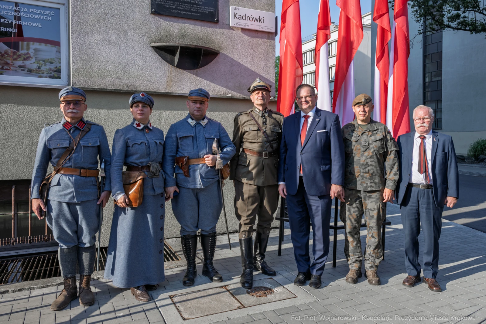 Grupa osób w mundurach historycznych oraz garniturach, z flagami w tle.  Autor: Piotr Wojnarowski