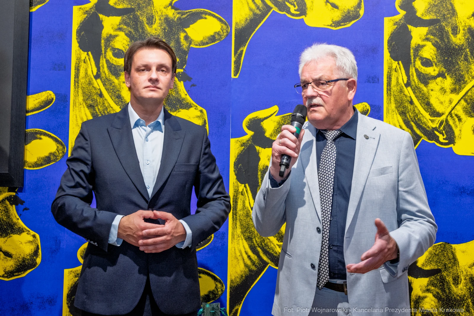 Dwaj mężczyźni podczas wystąpienia, w tle kolorowa grafika z wizerunkiem krów.  Autor: Piotr Wojnarowski