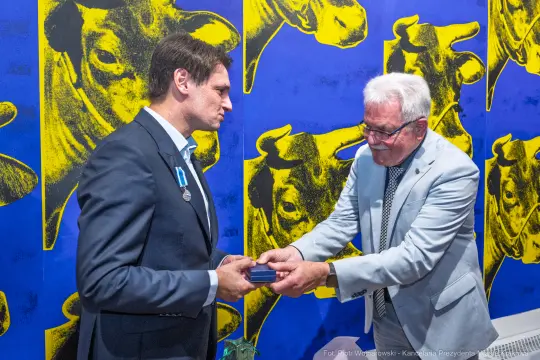 Mężczyźni wymieniają się odznaczeniami w tle z kolorowymi grafikami krów.