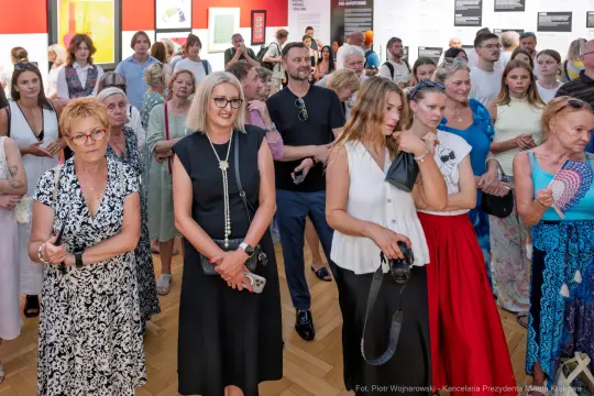 Grupa ludzi na wydarzeniu kulturalnym, różnorodne stroje i emocje uczestników.