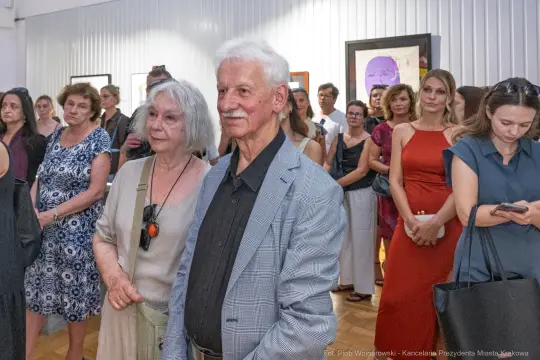 Grupa ludzi na wydarzeniu artystycznym, w tle prace na ścianach.