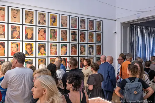 Wystawa portretów w galerii, ludzie oglądają prace artystyczne na ścianach.