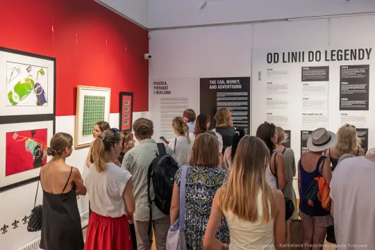 Wystawa z tłumem ludzi, eksponaty na ścianach dotyczące historii reklamy.