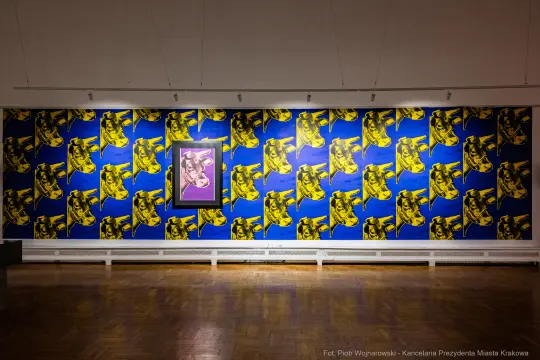 Ściana z kolorowymi grafikami oraz centralnym obrazem w ramie.