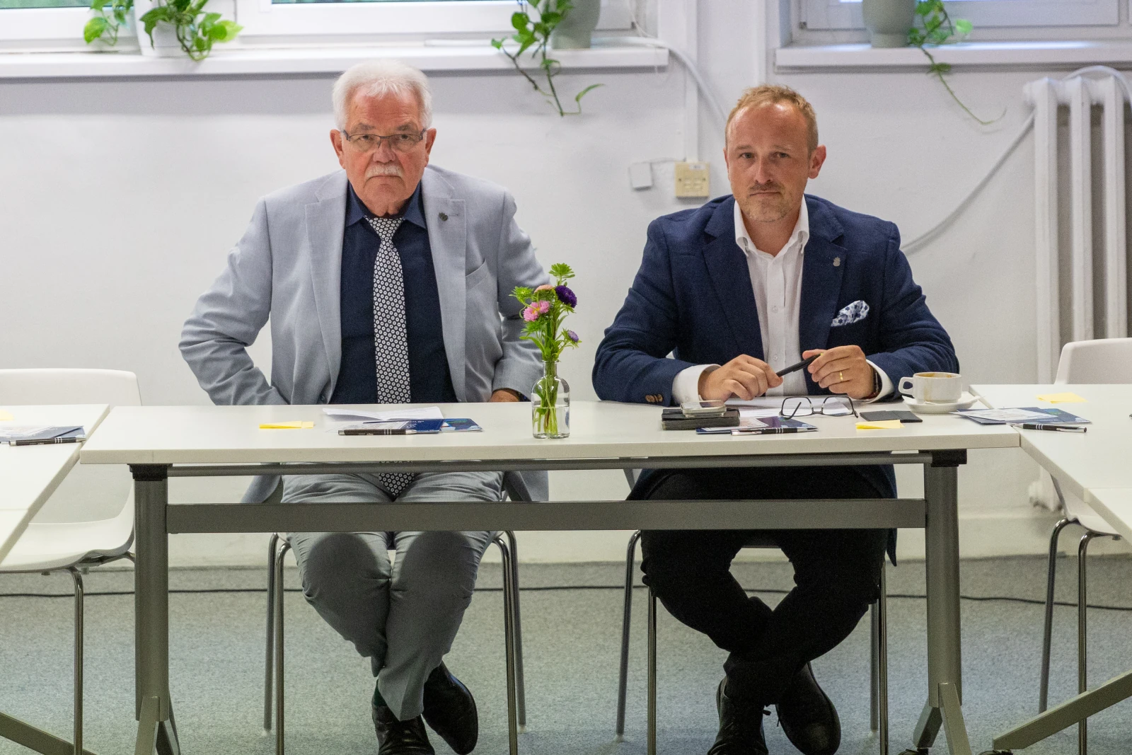 Dwaj mężczyźni siedzą przy stole, obok kwiatek w wazonie.  Autor: Bogusław Świerzowski