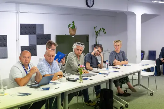 Grupa ludzi siedzących przy stole, prowadzących dyskusję w biurze.