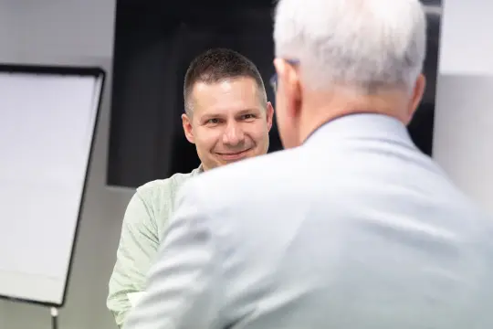Dwóch mężczyzn rozmawia w biurze, jeden z nich uśmiecha się.