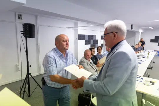 Mężczyzna odbierający dyplom od drugiego mężczyzny w sali konferencyjnej.