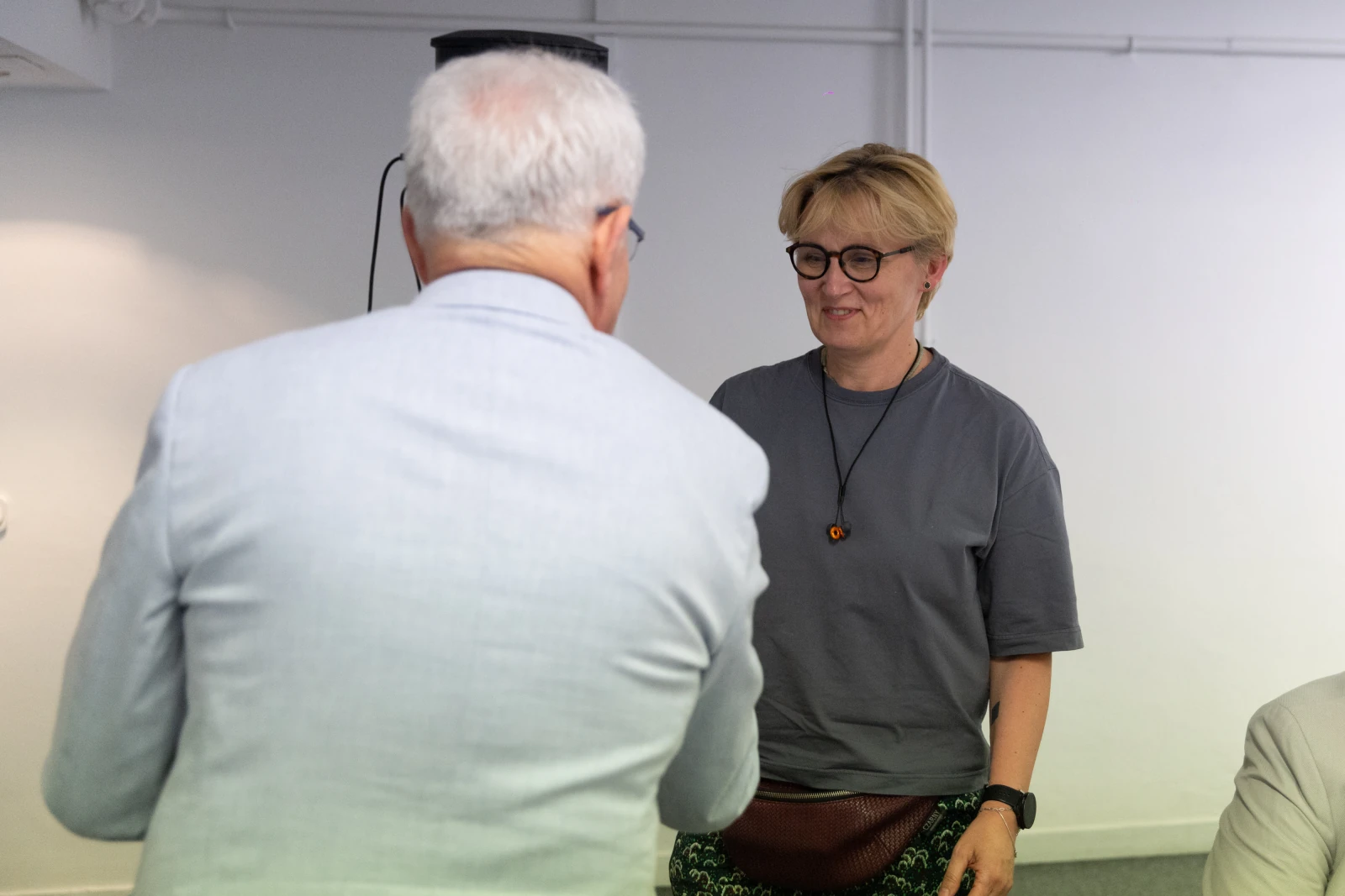 Spotkanie dwóch osób, jedna z nich uśmiecha się, druga wita ją.  Autor: Bogusław Świerzowski