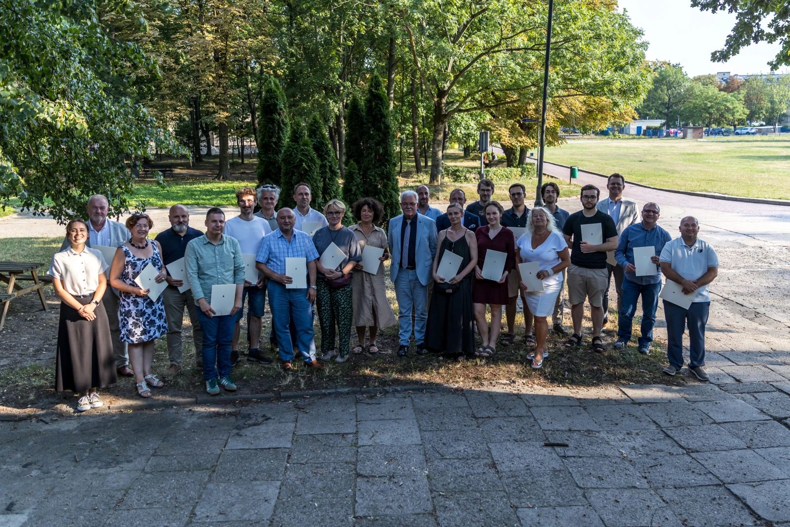 Grupa ludzi pozujących na zewnątrz, trzymających dyplomy lub certyfikaty.  Autor: Bogusław Świerzowski