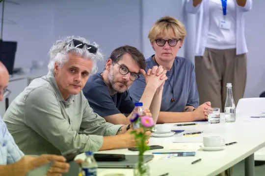Grupa osób siedzących przy stole, skupionych na dyskusji.