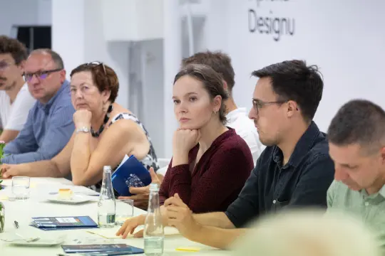 Grupa ludzi siedzących przy stole, skupionych na dyskusji.